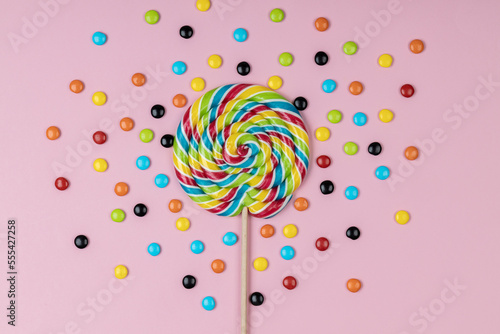 Sweet lollipop and colorful candy pills on pink background.