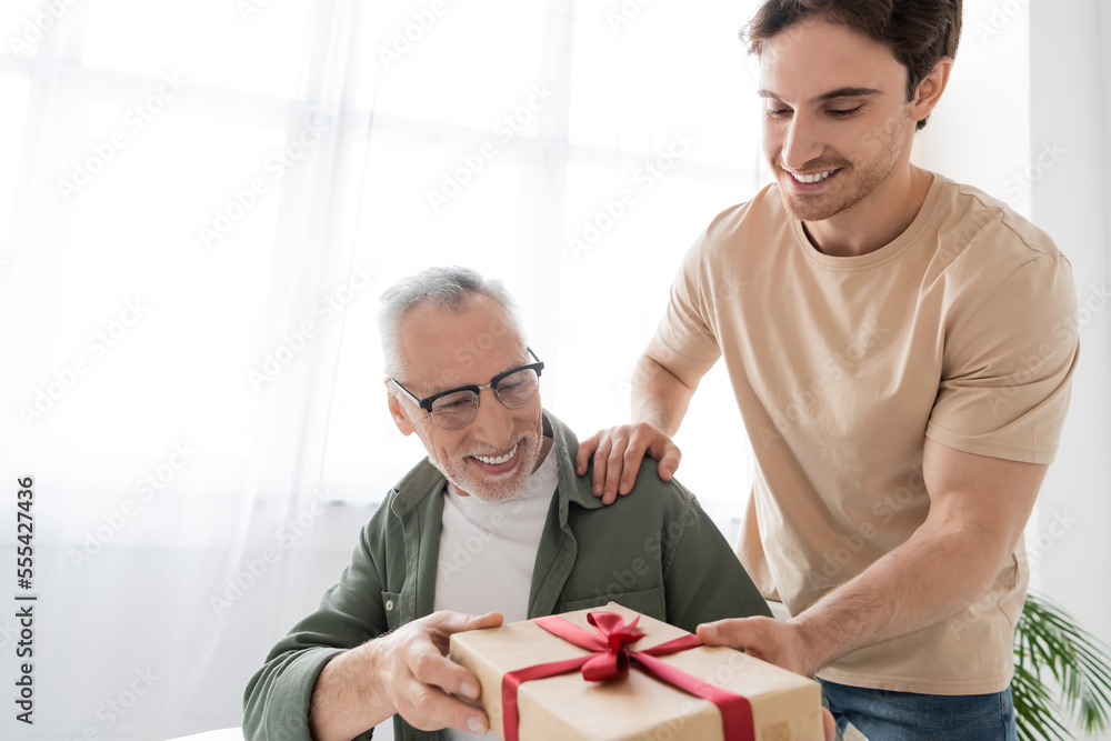 young man giving gift box to happy dad while congratulating him on ...