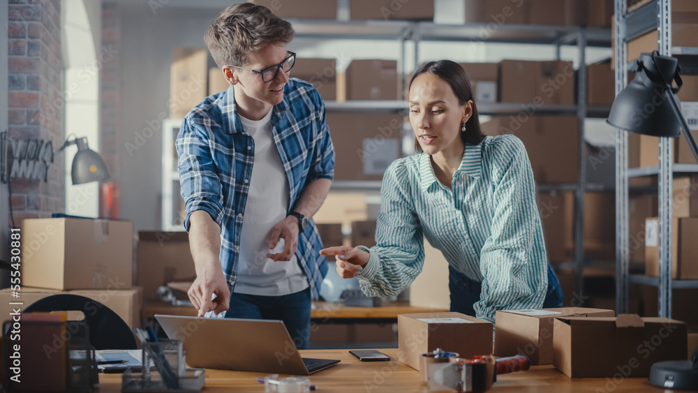 Positive Young Male and Female Working in Warehouse. Talking, Using Laptop Computer, Checking Retail Stock, Preparing Shipment. Successful Small Business Owners High Five Each Other. Positive Young Male and Female Working in Warehouse. Talking, Using Laptop Computer, Checking Retail Stock, Preparing Shipment. Successful Small Business Owners High Five Each Other.