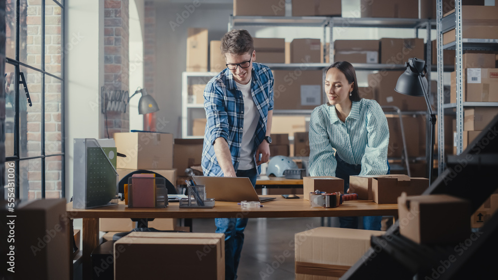 Positive Young Male and Female Working in Warehouse. Talking, Using Laptop Computer, Checking Retail Stock, Preparing Shipment. Successful Small Business Owners