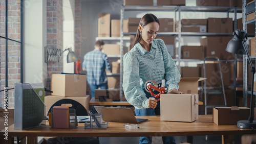 Stylish Storeroom Worker Preparing a Small Parcel for Postage. Inventory Manager Taping a Cardboard Box Before Shipping It to Customer. Female Small Business Owner Working in Warehouse Facility. © Gorodenkoff