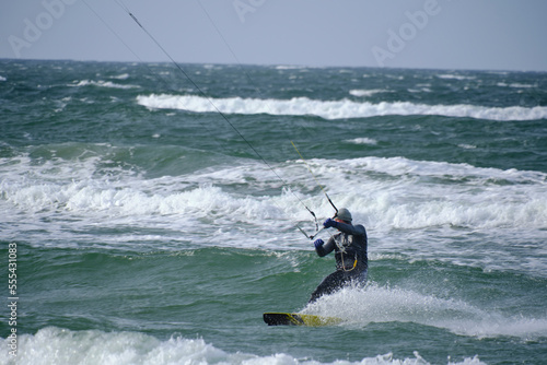 Kitesurfing, riding board waves during storm holding to flying kite.