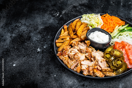 Shawarma Doner kebab on a plate with french fries and salad. Black background. Top view. Copy space