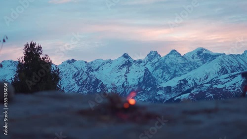 Landscape shot of snow covered Himalayan mountains in the morning with defocused bonfire burning in front of the mountains at Manali in Himachal Pradesh, India. Hiking background with campfire.  photo