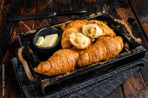Pile of French buttered croissants with butter in wooden tray. Wooden background. Top view