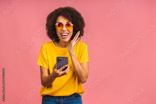 African american shocked amazed student woman using smartphone standing over isolated over pink background. Using mobile phone.