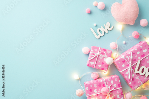Valentine's Day concept. Top view photo of gift boxes light bulb garland soft heart shaped toy inscriptions love and fluffy pompons on isolated pastel blue background with empty space