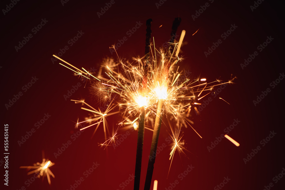 Two burning sparklers on a dark red background