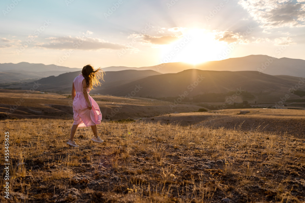 a girl in a pink dress walks across the field against the backdrop of mountains. a girl in a pink dress walks across the field against the backdrop of mountains.