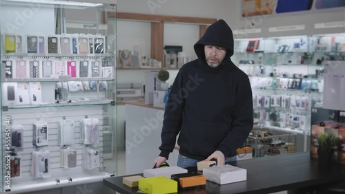 Suspicious man steals in a gadget store. The thief hides the goods and runs away from the store. photo
