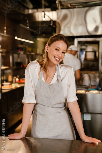 Cheerful woman chef cook standing in kitchen of a restaurant