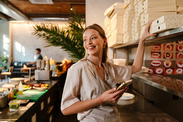 Smiling young woman preparing takeaway food in restaurant