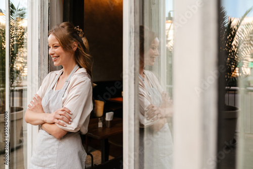 Young woman smiling while standing outdoors near restaurant with arms folded