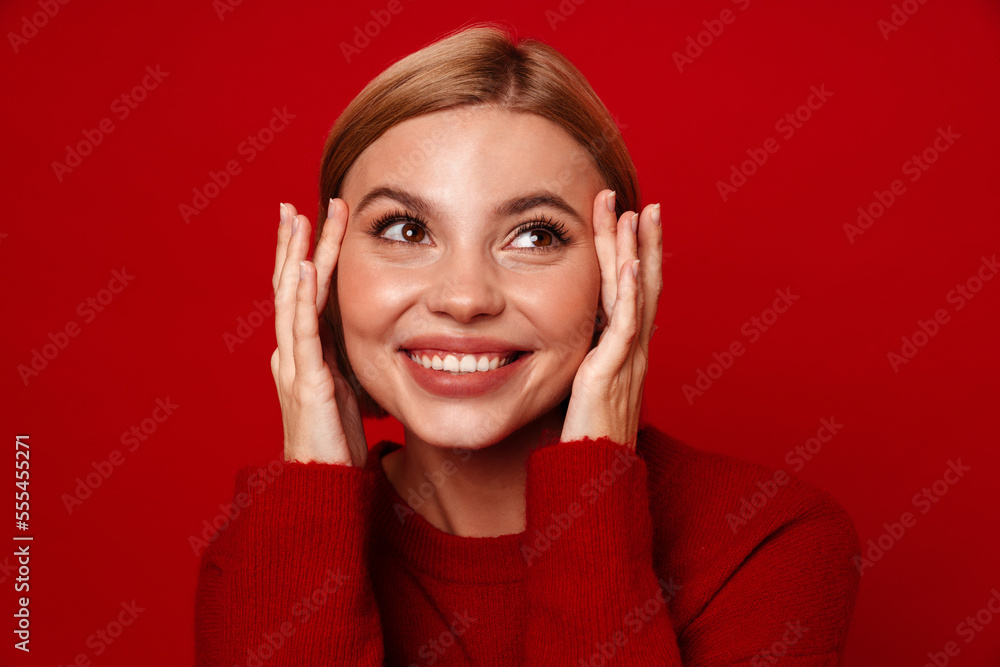 Smiling blonde woman touching her lips while standing isolated over red wall Smiling blonde woman touching her lips while standing isolated over red wall