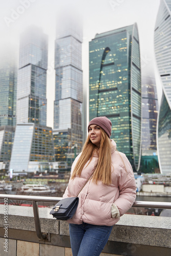 beautiful young woman in winter against the backdrop of high multi-storey skyscrapers in the clouds