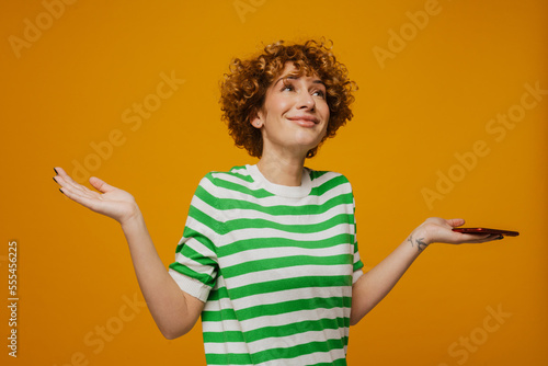 Curly ginger woman in striped t-shirt gesturing and using cellphone