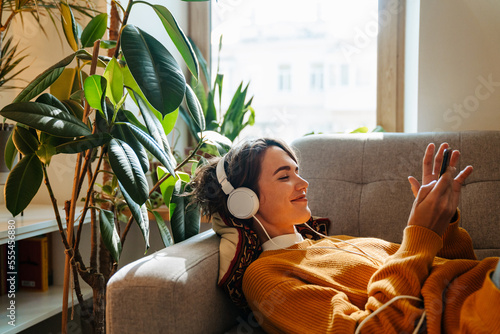 Εκτύπωση καμβά Young white woman in headphones using cellphone while lying on couch