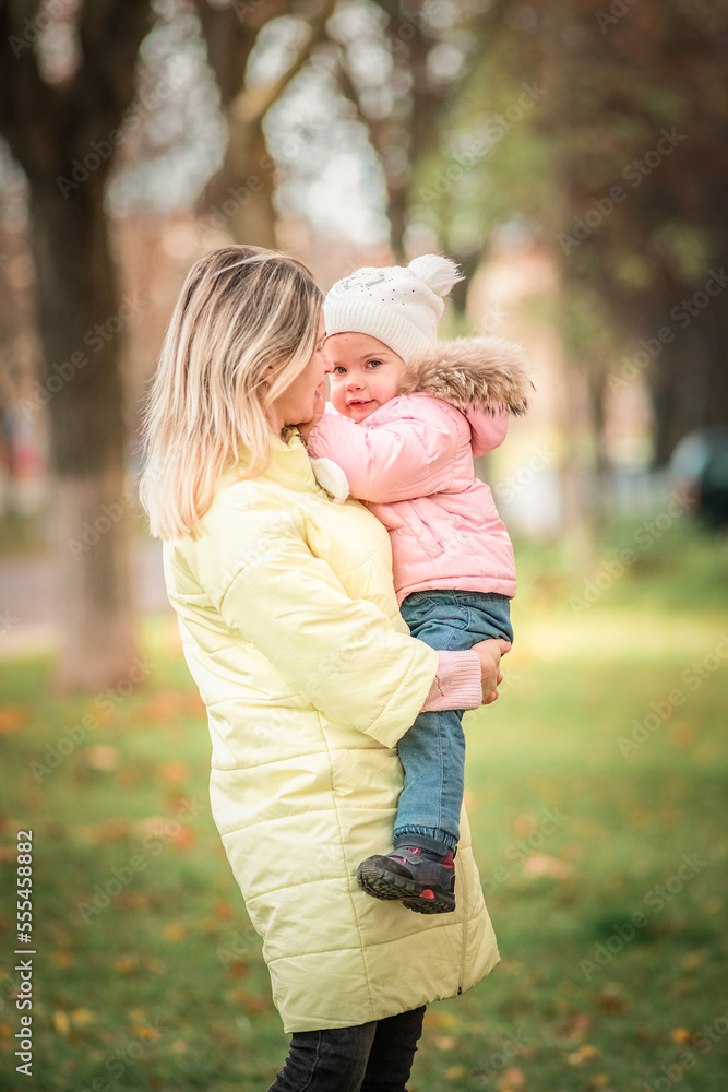 A young mother holds her daughter in her arms in the park in early spring. A young mother holds her daughter in her arms in the park in early spring.