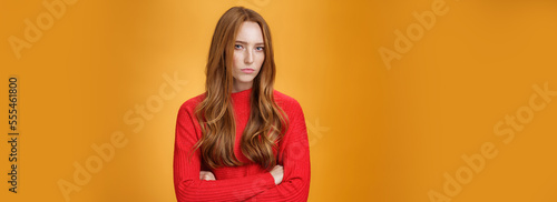 Suspicious intense and defensive ginger girl standing in passive-aggressive pose pouting and frowning looking with disbelief and disdain at camera, offended against orange background photo