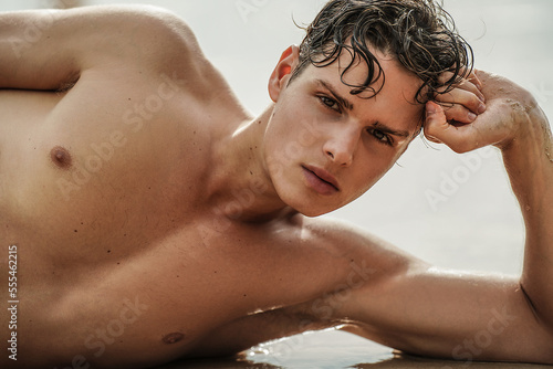 Portrait of handsome young Italian man posing on the beach, looking at the camera. Summer time. 