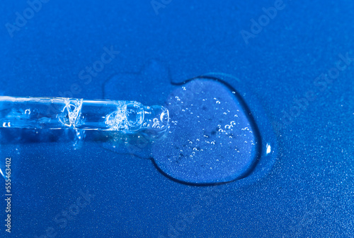 Transparent cosmetic drop with a glass pipette on a bright blue background with copy space. Beauty background with liquid transparent cosmetics. © Юлия Черкасова