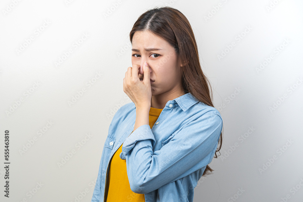 Portrait of pretty brunette hair, disgust smell bad strong asian young woman, girl hand squeezing, covering nose with fingers, expression face disgusting, dislike odor isolated on white background. Portrait of pretty brunette hair, disgust smell bad strong asian young woman, girl hand squeezing, covering nose with fingers, expression face disgusting, dislike odor isolated on white background.