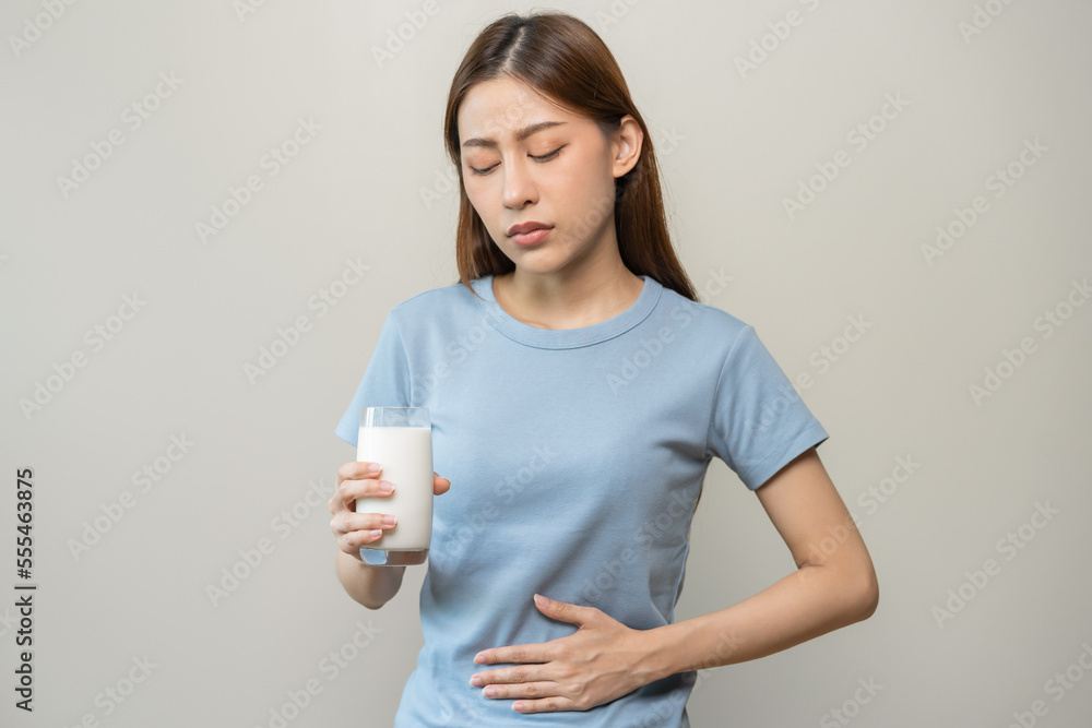 Pain, suffering asian young woman having a stomachache, abdominal pain or digestive, hand in holding belly after drink glass of milk. Lactose intolerance, allergy from dairy food, health care problem. Pain, suffering asian young woman having a stomachache, abdominal pain or digestive, hand in holding belly after drink glass of milk. Lactose intolerance, allergy from dairy food, health care problem.