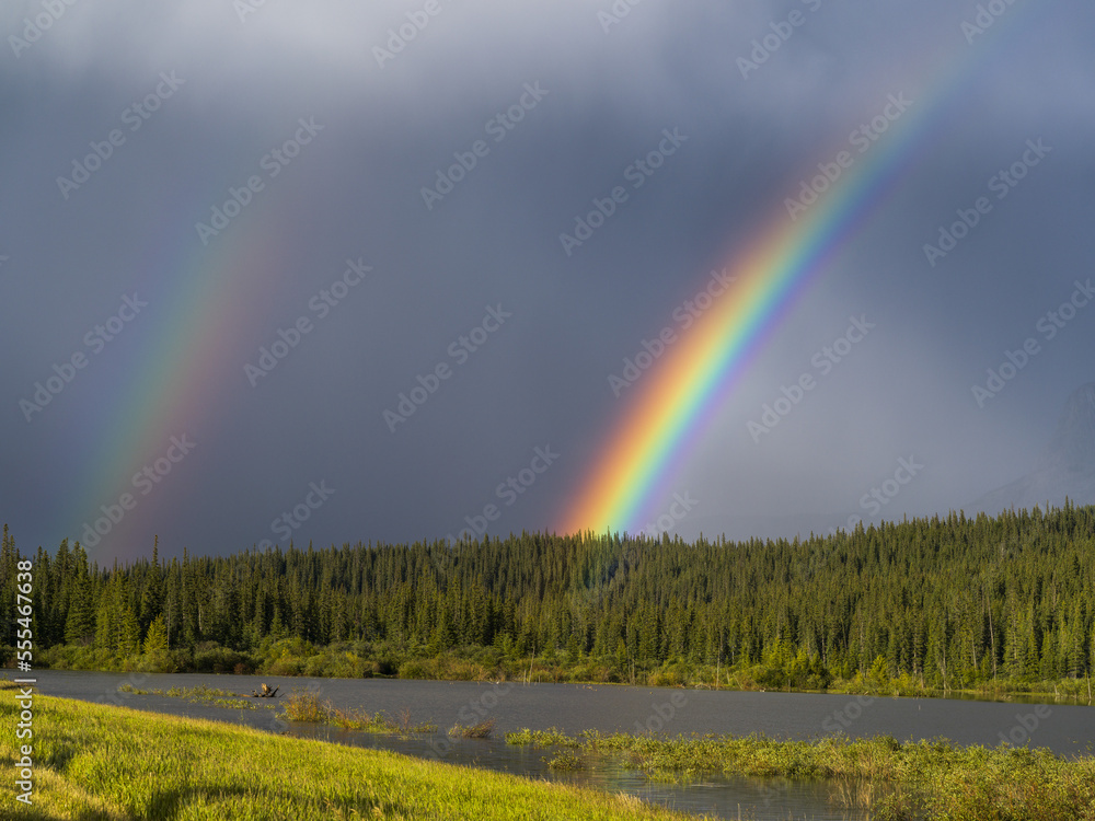 Double rainbow in storm clouds with a forest and river in the foreground; Alberta, Canada Double rainbow in storm clouds with a forest and river in the foreground; Alberta, Canada