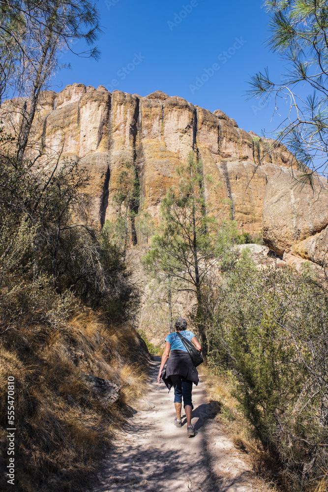 A woman walking up the Balconies Cave trail below massive cliffs in the Pinnacles National Park; California, United States of America A woman walking up the Balconies Cave trail below massive cliffs in the Pinnacles National Park; California, United States of America