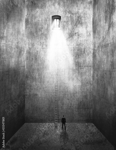 Image of a man standing in an empty room with tall walls and a ladder leading up to the sunlight streaming from a window far above, composite image photo