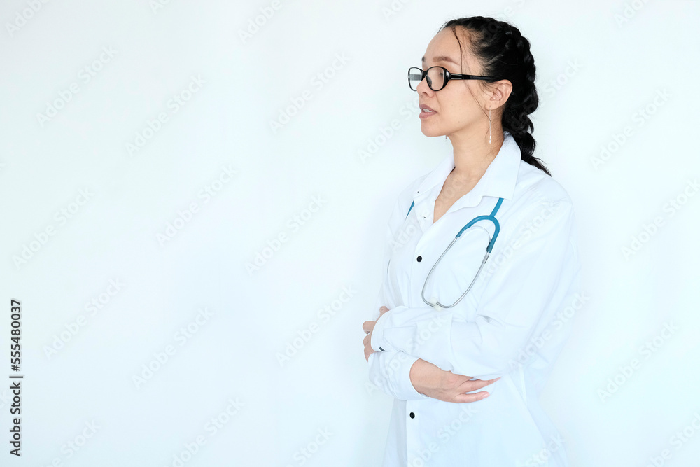 Image of confident female doctor wearing glasses, trainee with stethoscope and medical gown, arms crossed like a professional looking at camera confidently, against white background, Asian appearance 