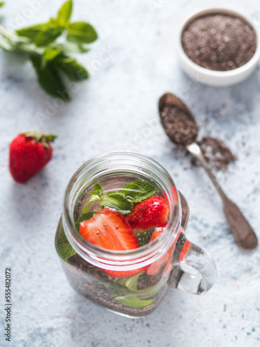 View from above chia water in mason jar with strawberry and mint on gray cement background. Chia infused detox water with berries. Healthy eating, drinks, diet, detox concept. Vertical