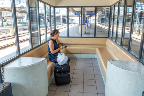 Female passenger using her smart phone while waiting for train with suitcase in Basel SBB railway station; Basel, Basel Stadt, Switzerland photo
