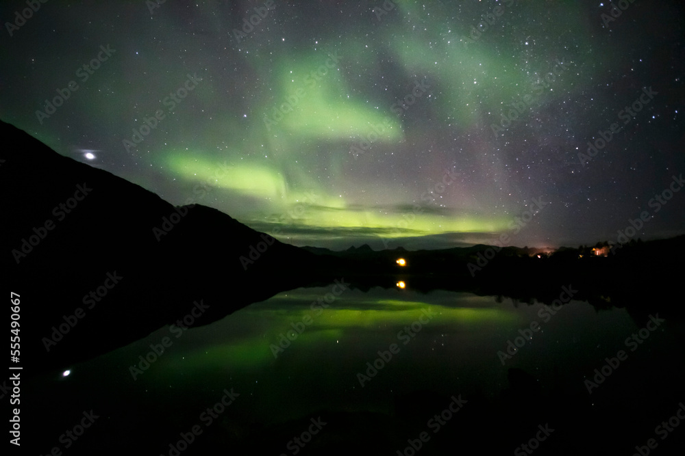 
Green northern lights in Lofoten islands, Norway. Aurora borealis. Starry sky with polar lights. Night landscape with aurora, sea with sky reflection and mountains. Nature. Travel