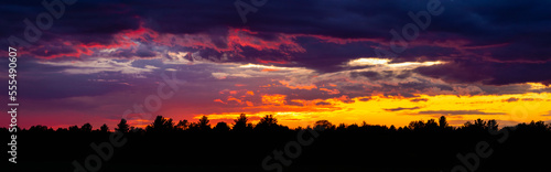 Dramatic sky at sunset with dark clouds and colourful light glowing above silhouetted trees; Bromont, Quebec, Canada photo