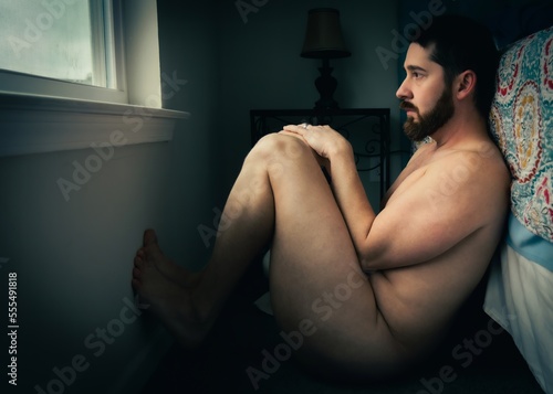 Fotografija artistic realism nude male sitting on floor against bed looking out window
