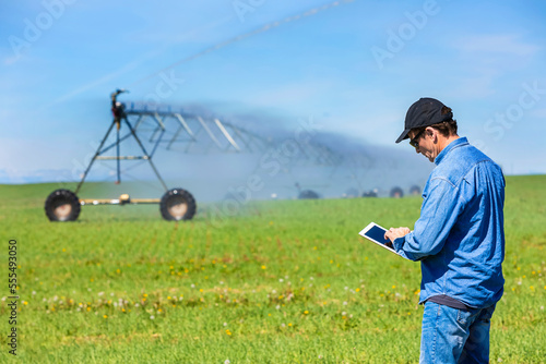 Farmer using a tablet on a farm field with irrigation; Alberta, Canada
