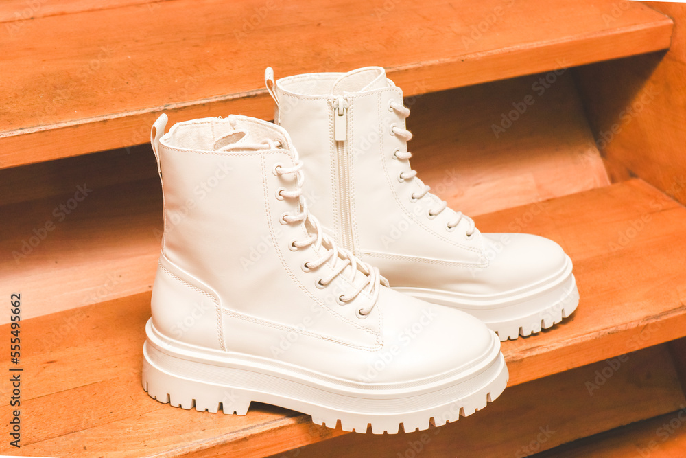 White demi-season boots made of eco-leather with fasteners, laces and rough sole on wooden steps. White demi-season boots made of eco-leather with fasteners, laces and rough sole on wooden steps.