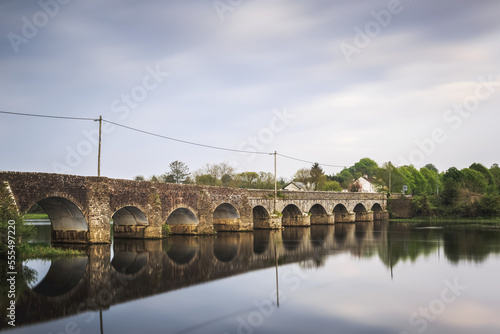 O'Briens Bridge, an old stone bridge crossing the River Shannon with it's reflection in the water; County Clare, Ireland