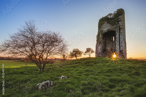 Old Irish castle ruins in a green field with the setting sun coming through the window hole; Clonlarra, County Clare, Ireland photo