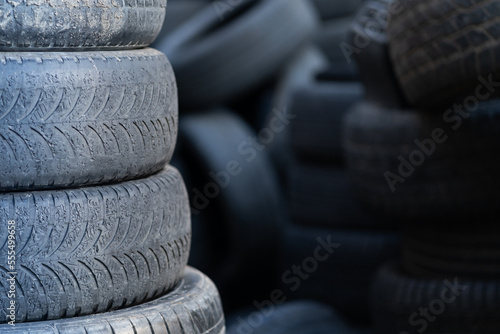 Closeup of old used rubber tires stacked with high piles, blurred background and copy space. Tyre dump. Hazardous waste requiring recycling and disposal. 