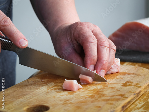 Hands of a seigners woman cutting a raw pork meat fillet on a wooden board with a knife