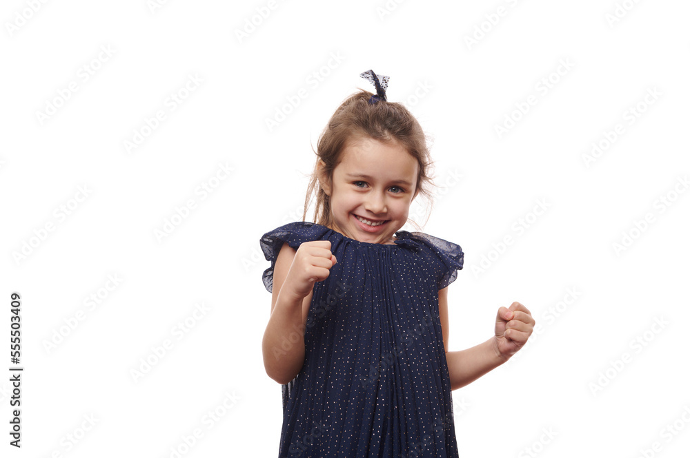 Emotional portrait Caucasian mischievous little child girl in beautiful elegant blue dress, clenching fists and cutely smiling looking at camera, isolated over white background. Copy advertising space Emotional portrait Caucasian mischievous little child girl in beautiful elegant blue dress, clenching fists and cutely smiling looking at camera, isolated over white background. Copy advertising space