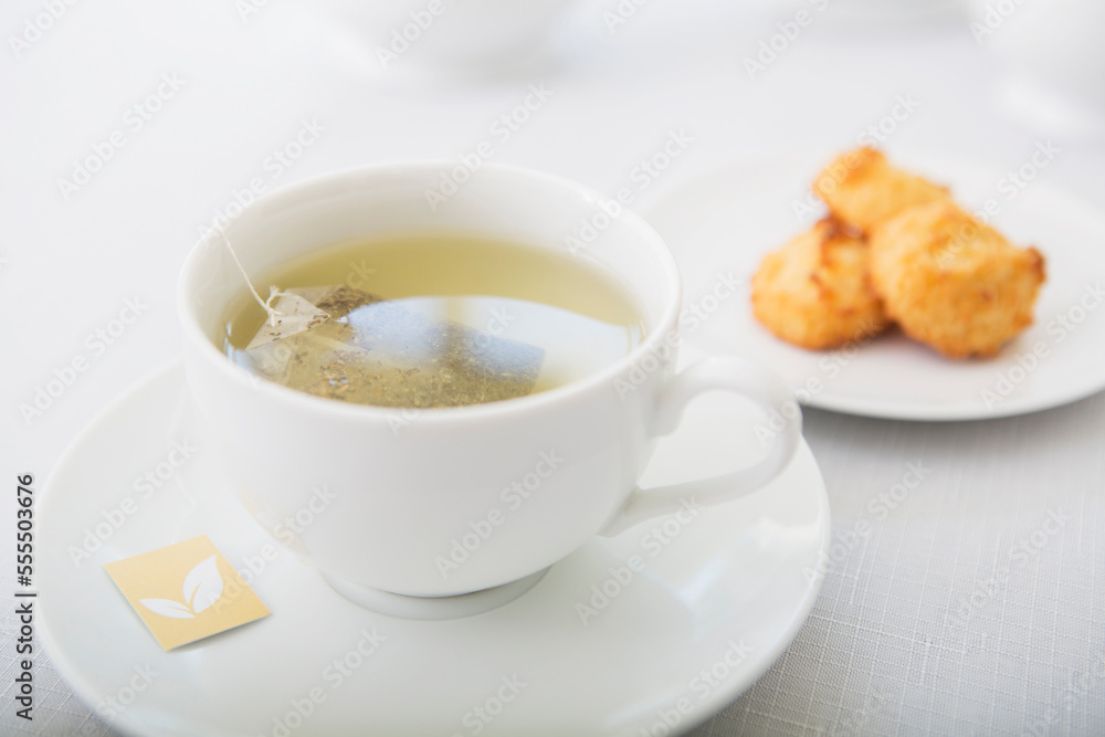 Cup of tea in porcelain white teacup with saucer and plate of coconut macaroons, studio shot Cup of tea in porcelain white teacup with saucer and plate of coconut macaroons, studio shot