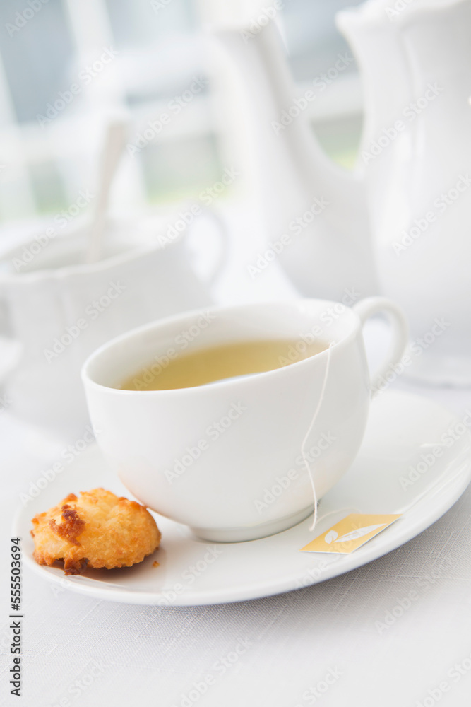 Cup of tea in porcelain white teacup with saucer, sugar bowl, teapot and plate of coconut macaroons, studio shot Cup of tea in porcelain white teacup with saucer, sugar bowl, teapot and plate of coconut macaroons, studio shot