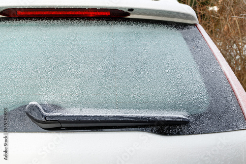 Snow on frozen window of parking white car in winter