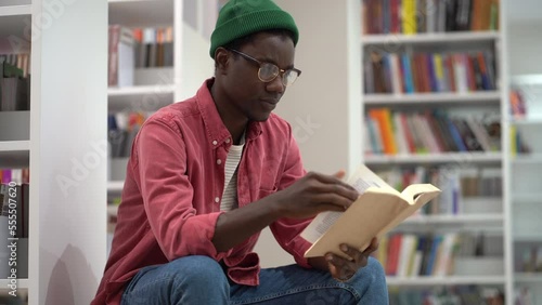 Smart focused African American male student carefully studying book turning pages sits indoors in bookstore. Young black guy is passionate about reading favorite fiction novel with exciting plot