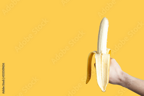 Banana as a symbol of the male penis in the hand isolated on yellow background. Sexual masturbation and orgasm, impotence problem. The concept of self-satisfaction.