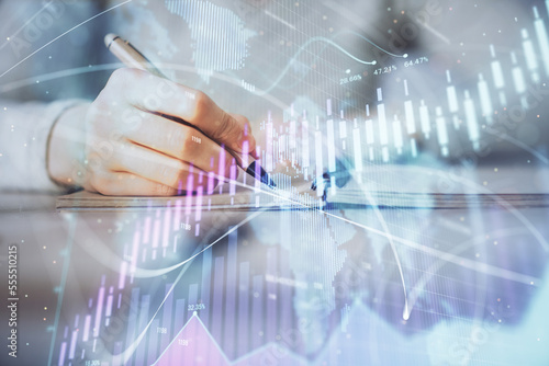 Hands writing information about stock market in notepad. Forex chart holograms in front. Concept of research. Multi exposure