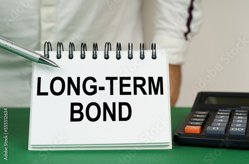 On a green surface, a calculator and a notepad with the inscription - Long-Term Bond